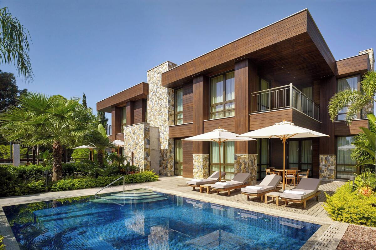 A modern hotel with a swimming pool, lounge chairs, and umbrellas.