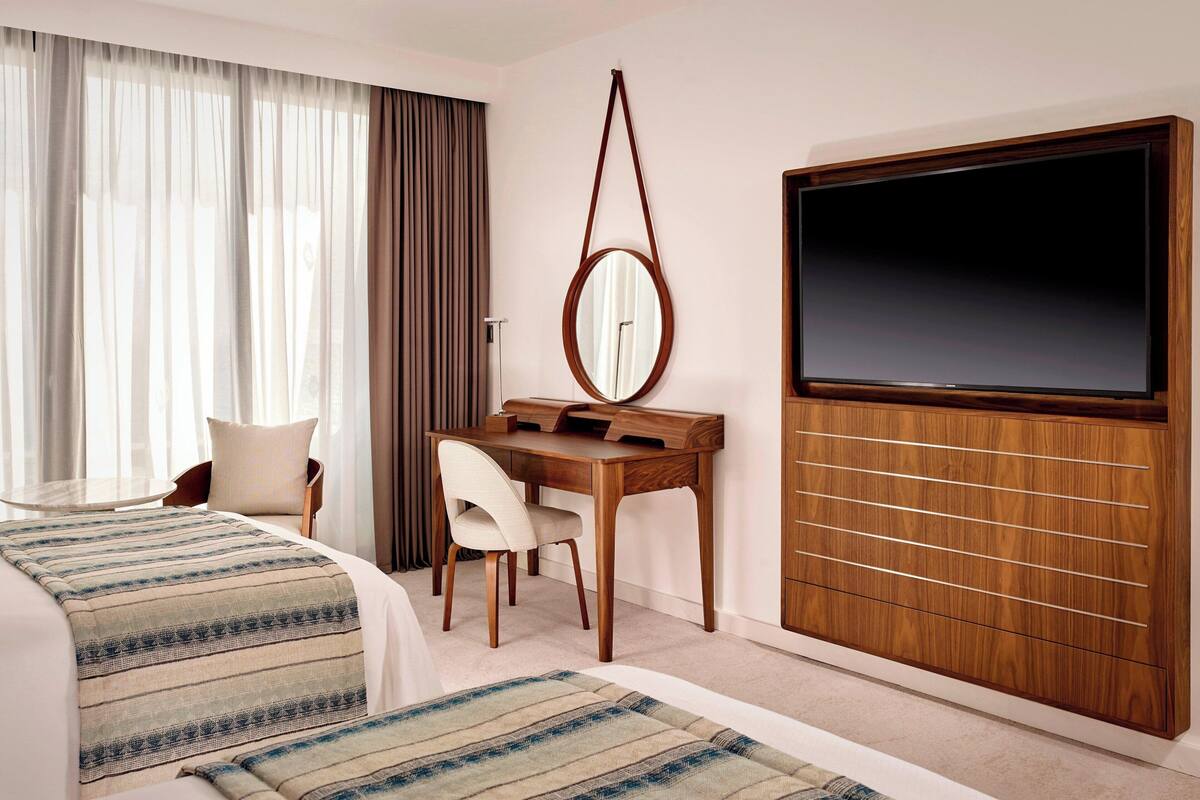 A hotel room with a bed, a desk, a chair, a TV, and a large mirror.