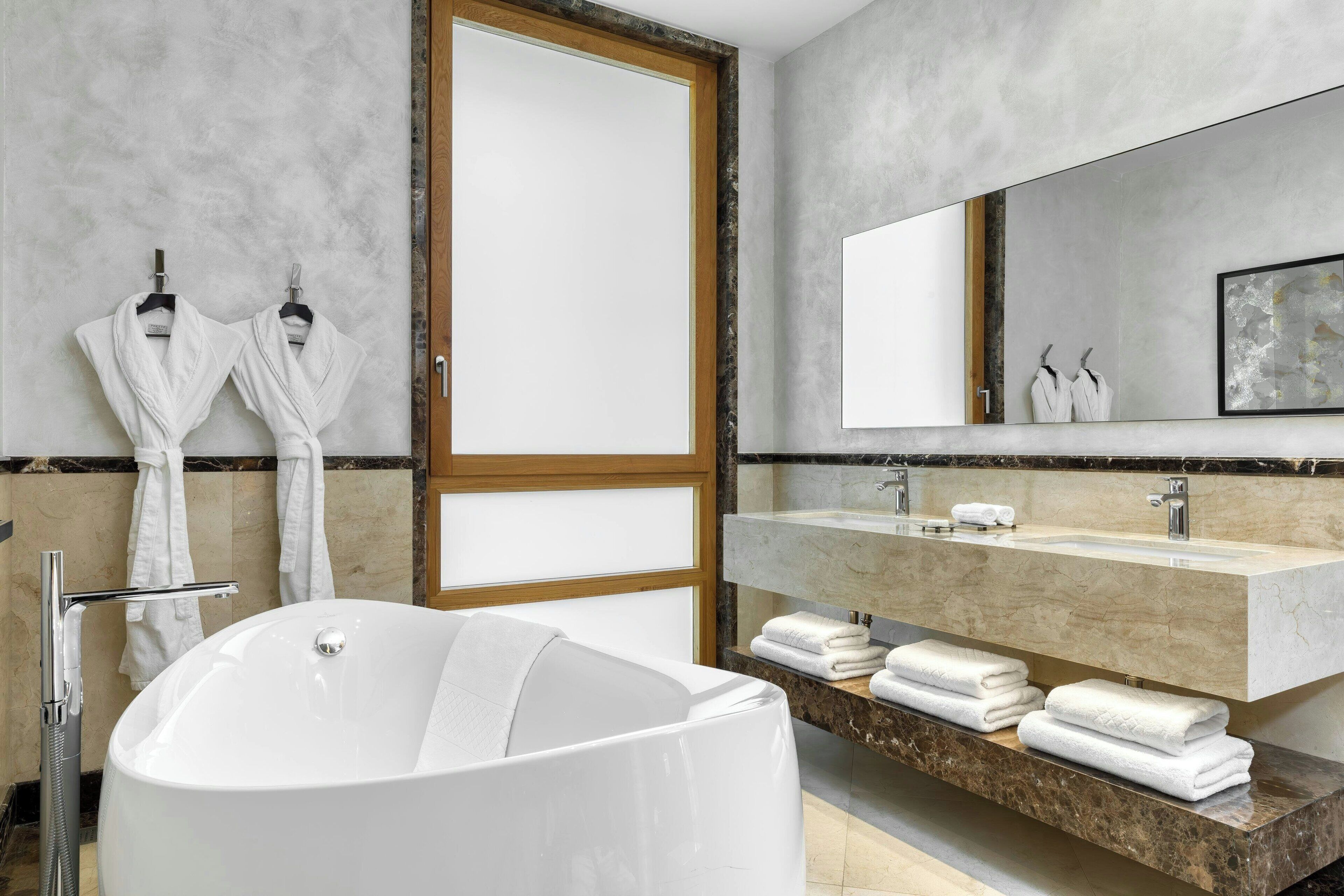 A modern bathroom with a freestanding bathtub, a large mirror, and a marble countertop.