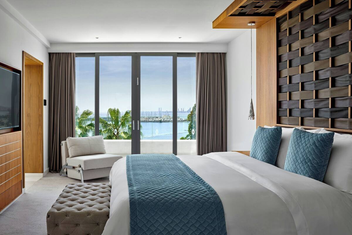 A modern hotel room with a large bed, a sofa, a TV, and a balcony with a city view.