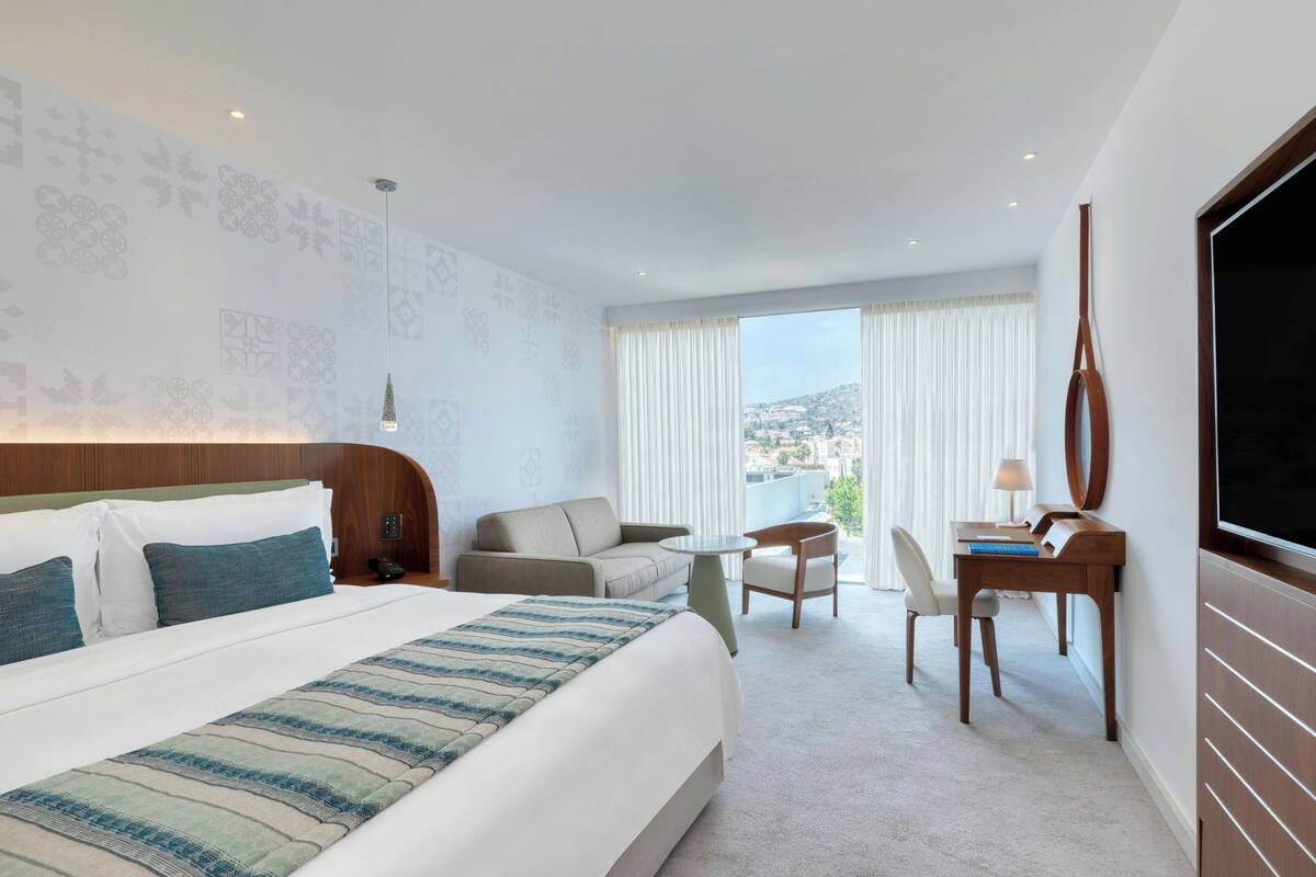 A hotel room with a large bed, a sofa, a small table, a chair, and a TV.