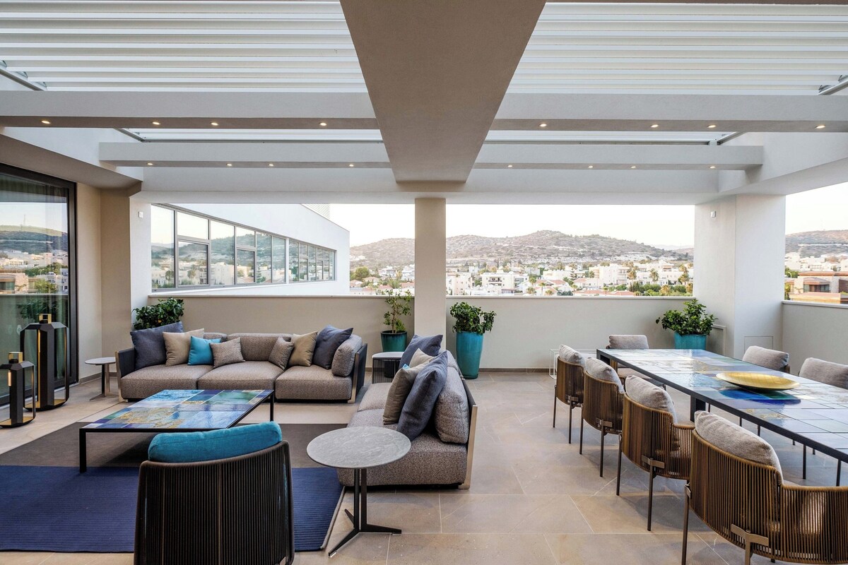 A rooftop terrace with a sofa set, dining table, chairs, and potted plants.