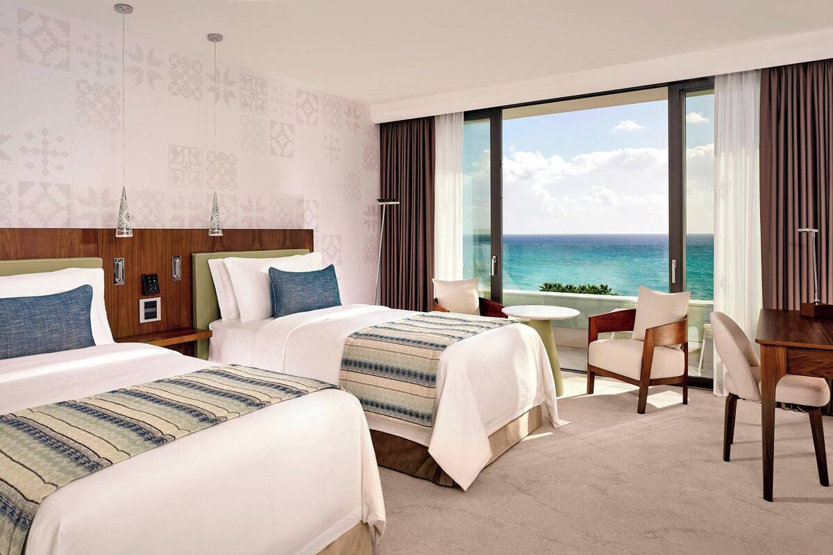 A hotel room with two beds, a desk, and a view of the ocean.