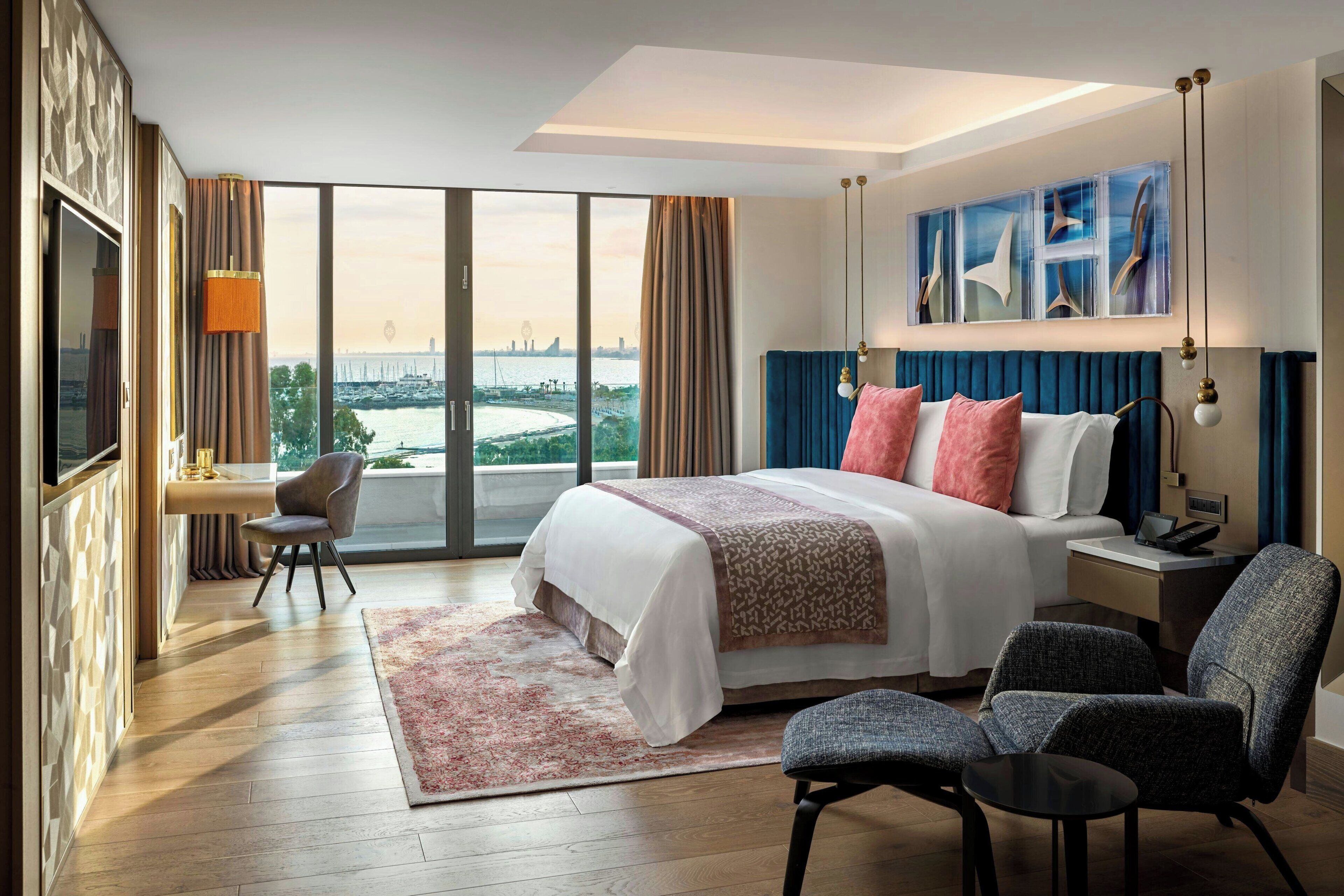 A hotel room with a large bed, a desk with a chair, a TV, and a view of a cityscape.