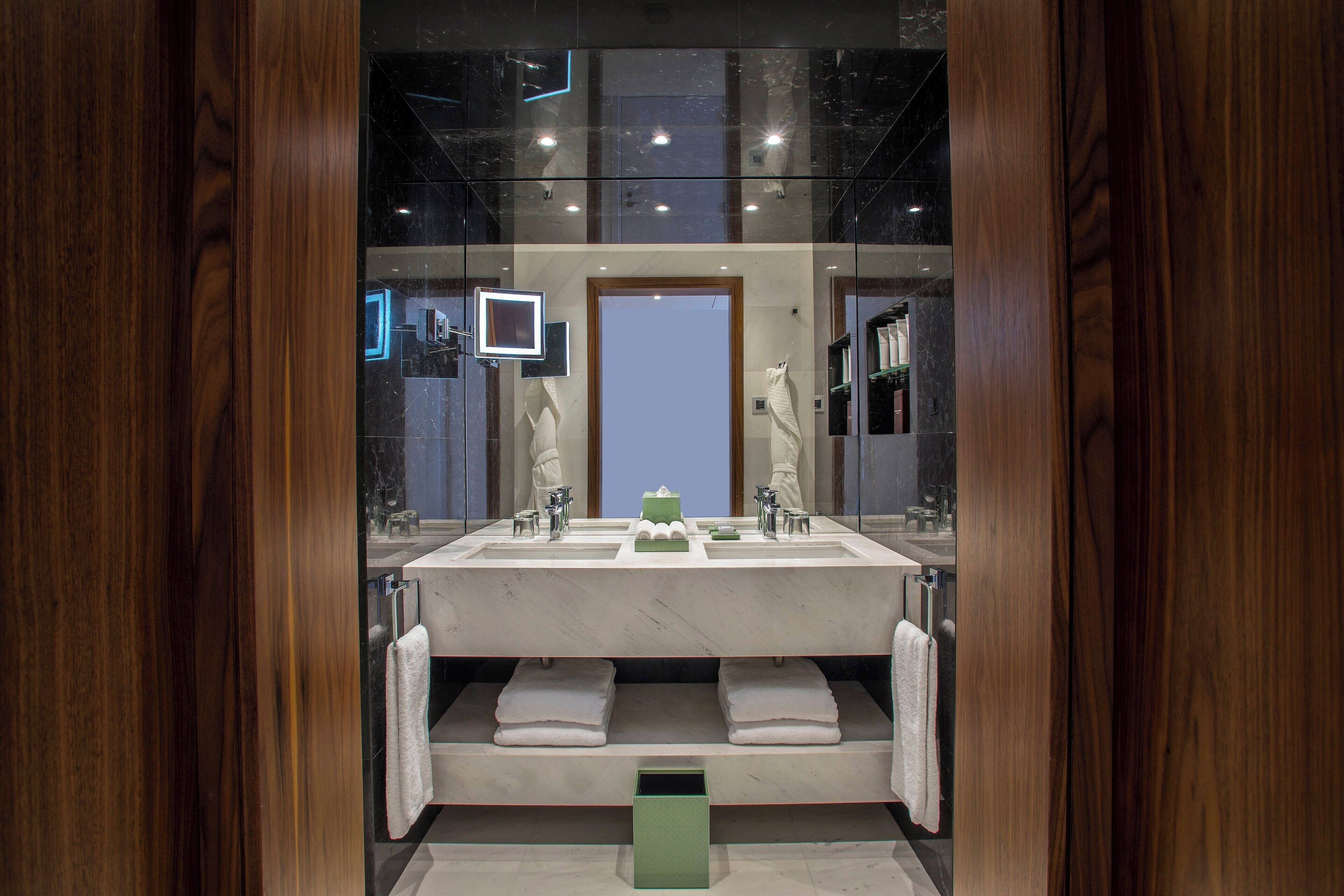 Une salle de bain moderne avec un grand miroir, deux lavabos et une poubelle verte.