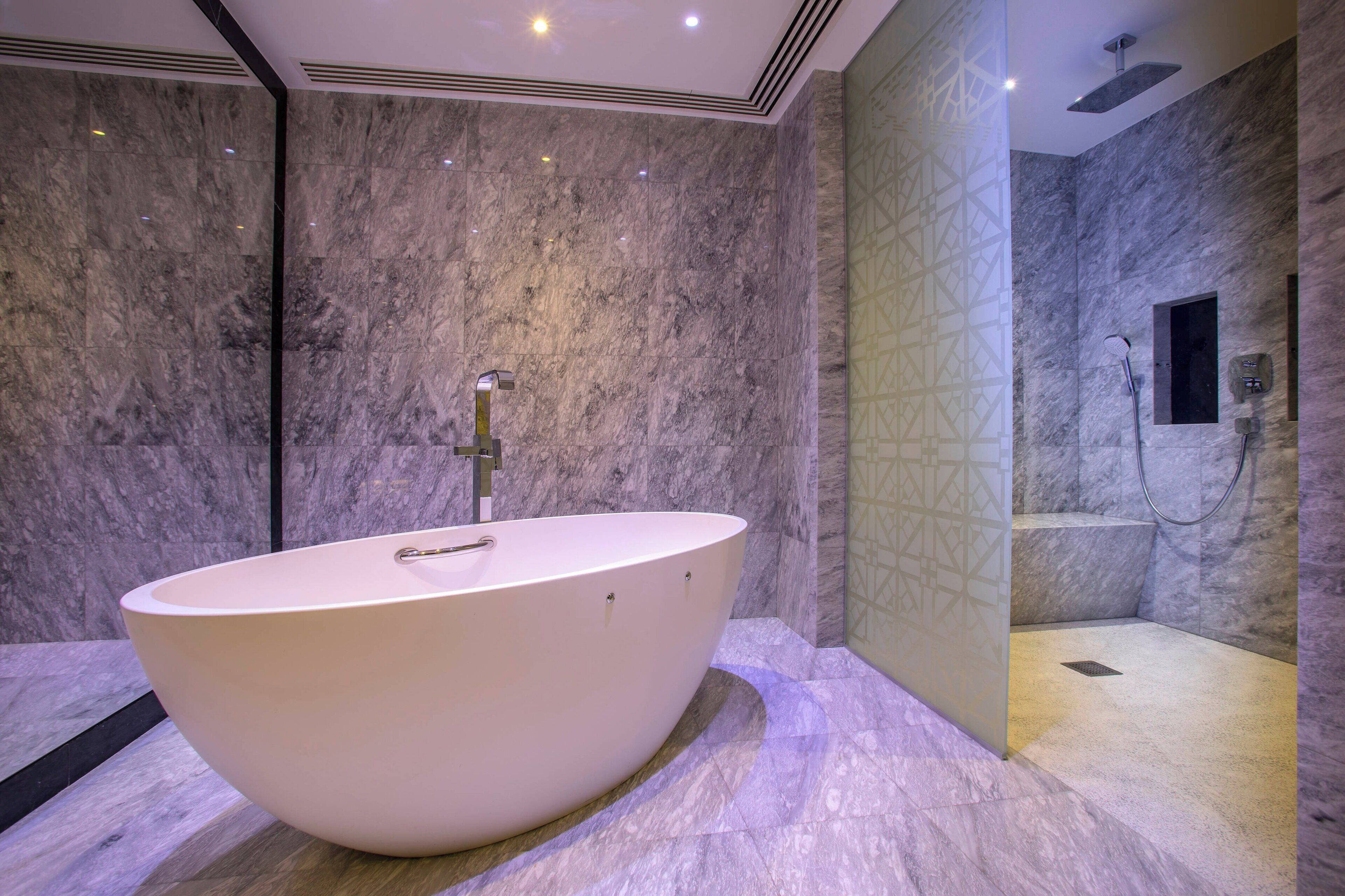Un bagno moderno con una vasca freestanding, una zona doccia e pareti in marmo.