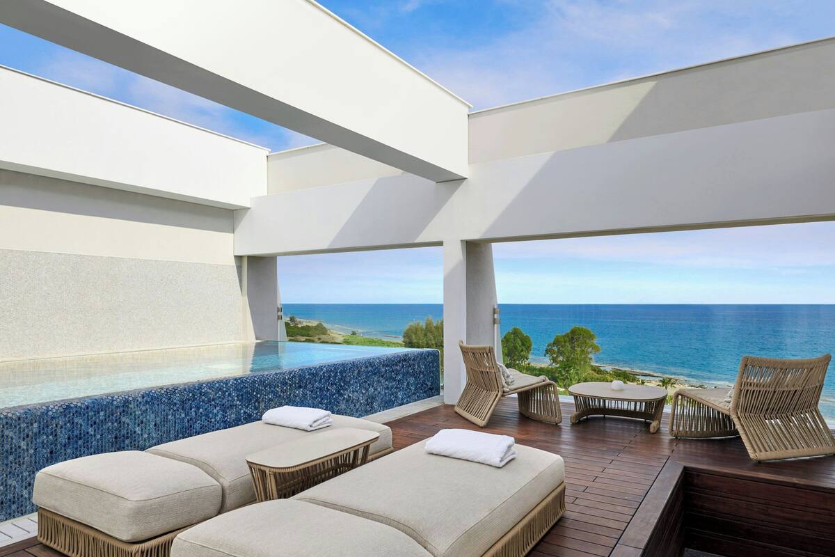A modern outdoor lounge area with a pool, lounge chairs, and a view of the ocean.