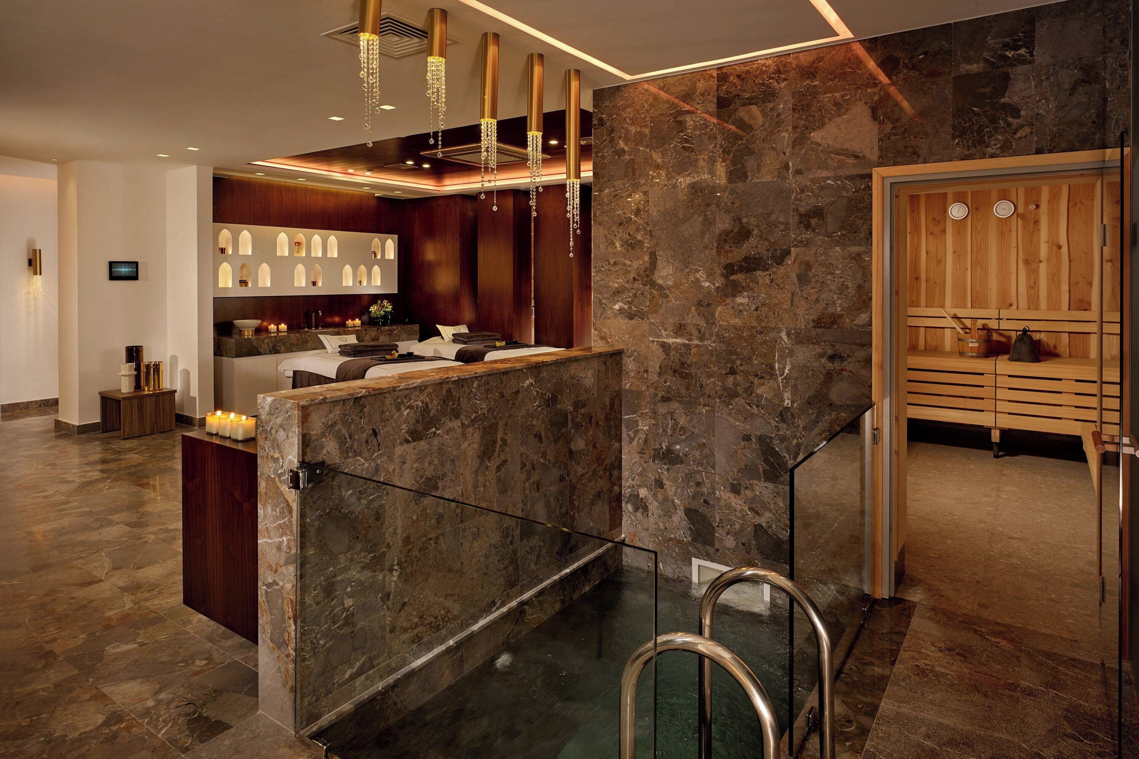 A modern hotel lobby with a reception desk, a seating area with a wooden bench, and a stone wall.