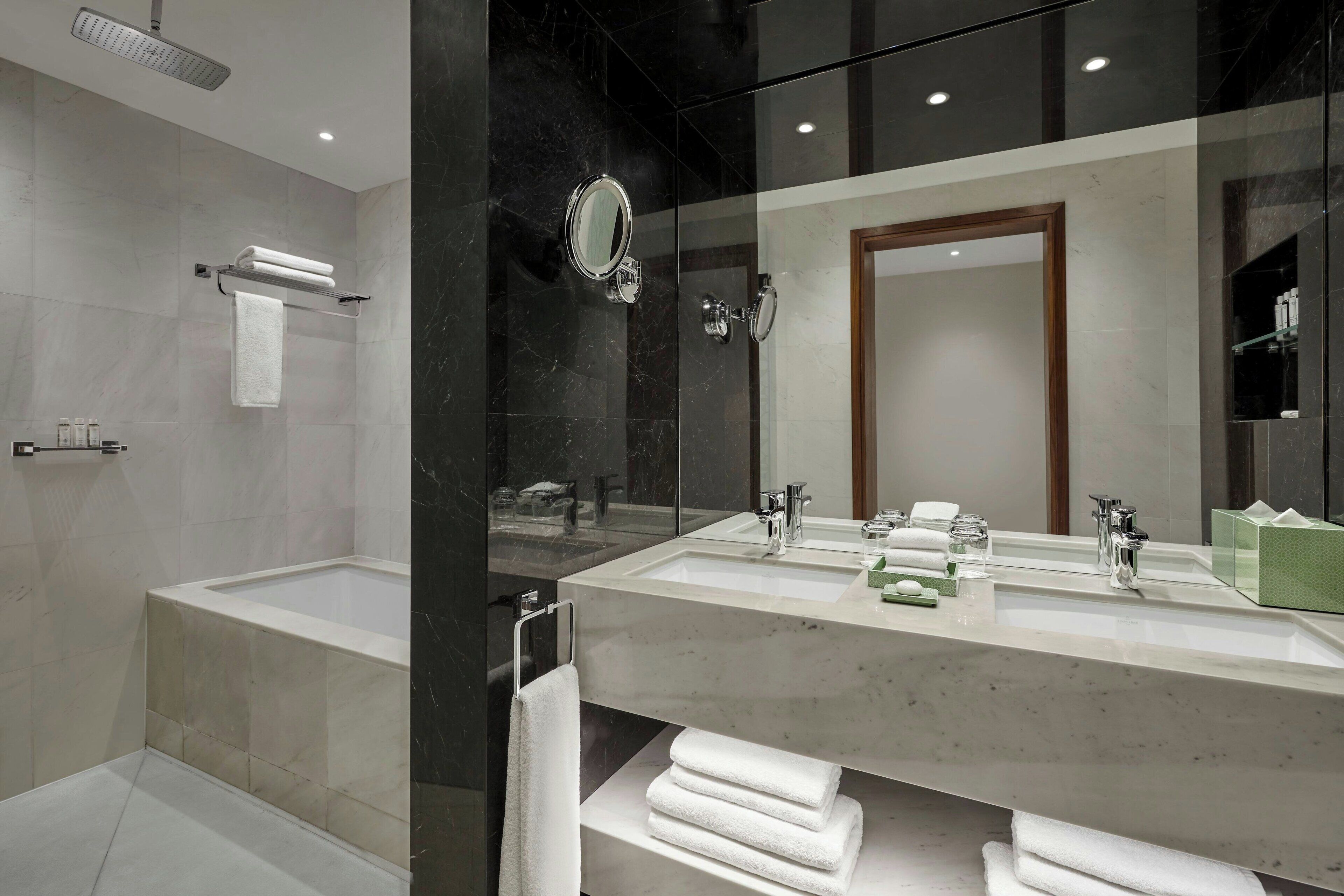 Een moderne badkamer met een grote spiegel, twee wasbakken, een douche en keurig opgevouwen handdoeken.