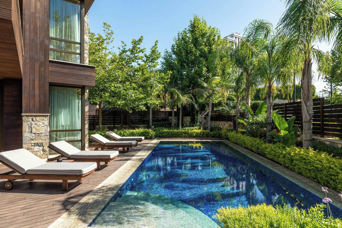 A swimming pool with lounge chairs, surrounded by greenery and a stone wall.