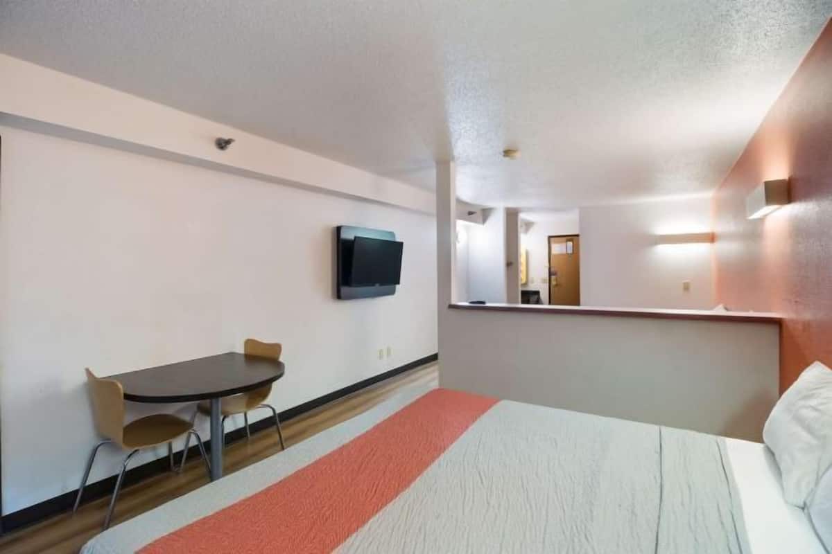 A hotel room with a bed, a desk with a chair, a television mounted on the wall, and a mirror above the desk.
