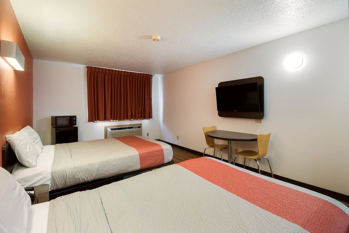 A hotel room with two beds, a TV, a small table with chairs, and a microwave.