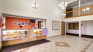 Zona de recepción de un hotel con un mostrador de check-in, un mapa en la pared y una escalera a un nivel superior.