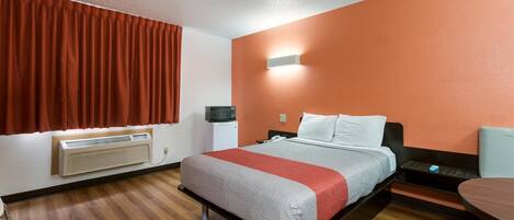 A hotel room with a bed, a bedside table, a chair, a heater, and a window with curtains.