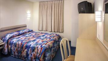 Habitación de hotel con cama, una silla, escritorio, televisión y ventana con cortinas.