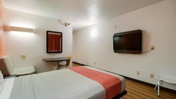 A hotel room with a bed, a desk, a chair, a television, and a window with curtains.