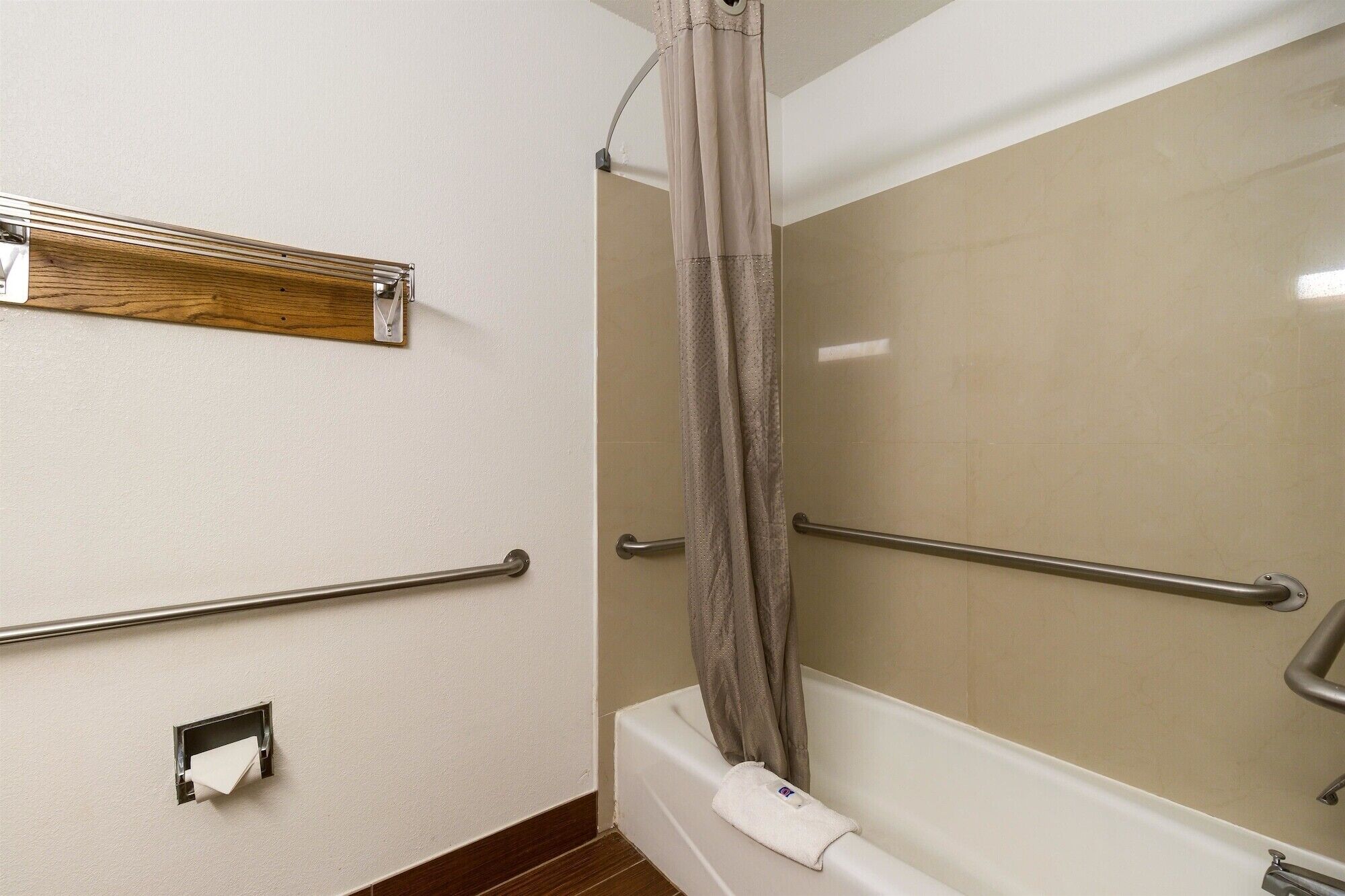 A bathroom with a shower, grab bars, a towel rack, and a toilet paper holder.