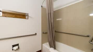 Un baño con ducha, barras de apoyo, toallero y soporte para papel higiénico.