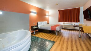 Habitación de hotel con una bañera grande, una cama con una manta roja, un escritorio y un televisor.