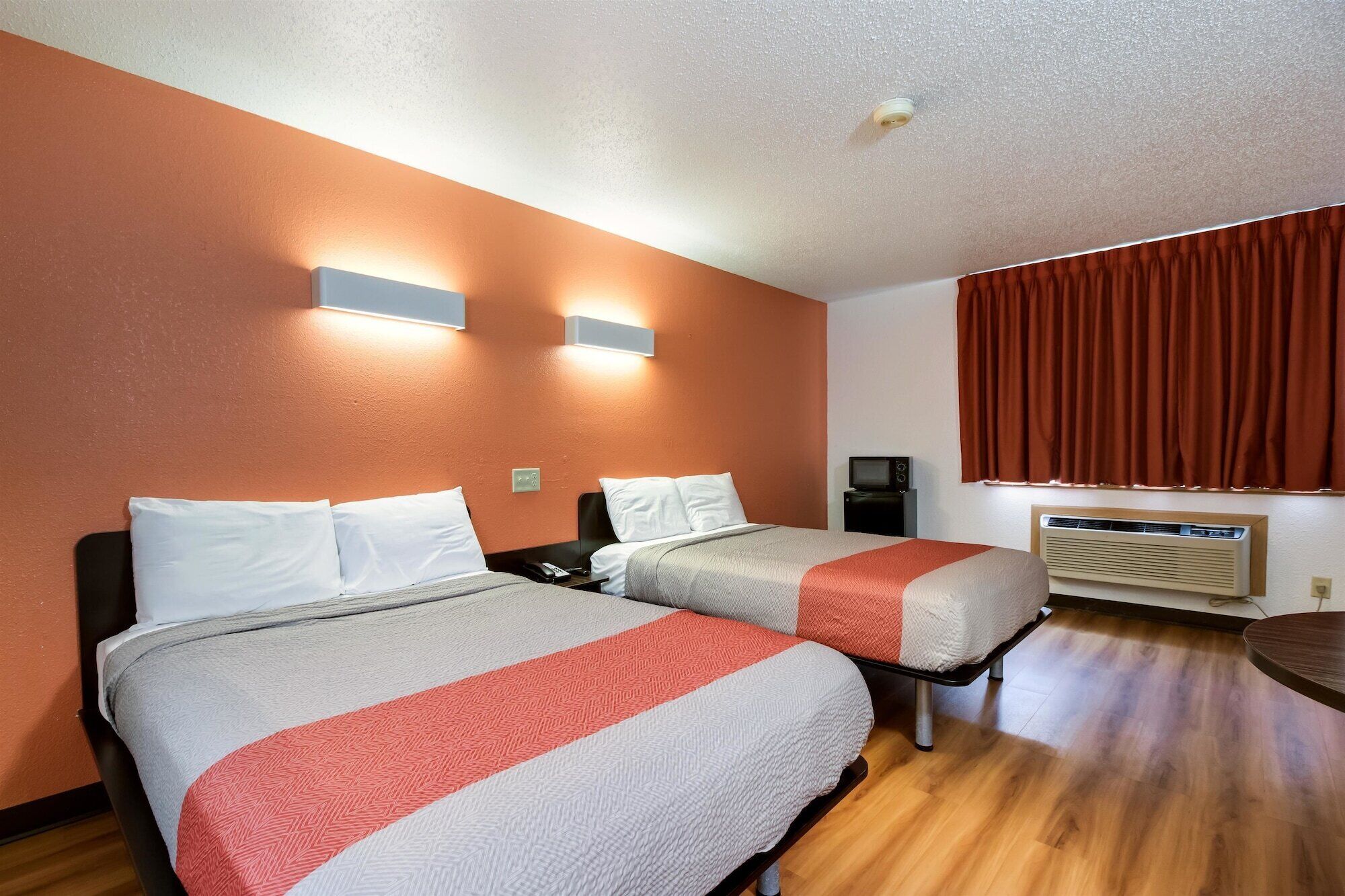 Habitación de hotel con dos camas, un escritorio, una silla, un calentador y una ventana con cortinas.