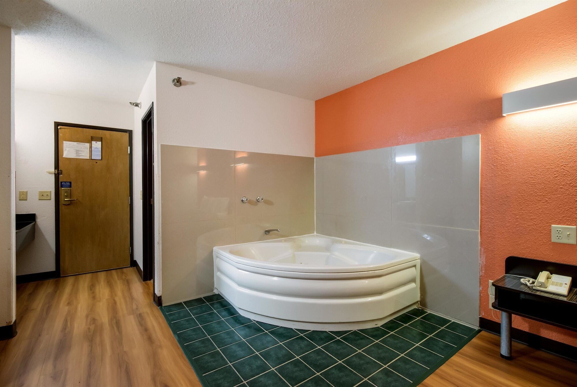 A bathroom with a large bathtub, a wooden floor, and a green-tiled floor.