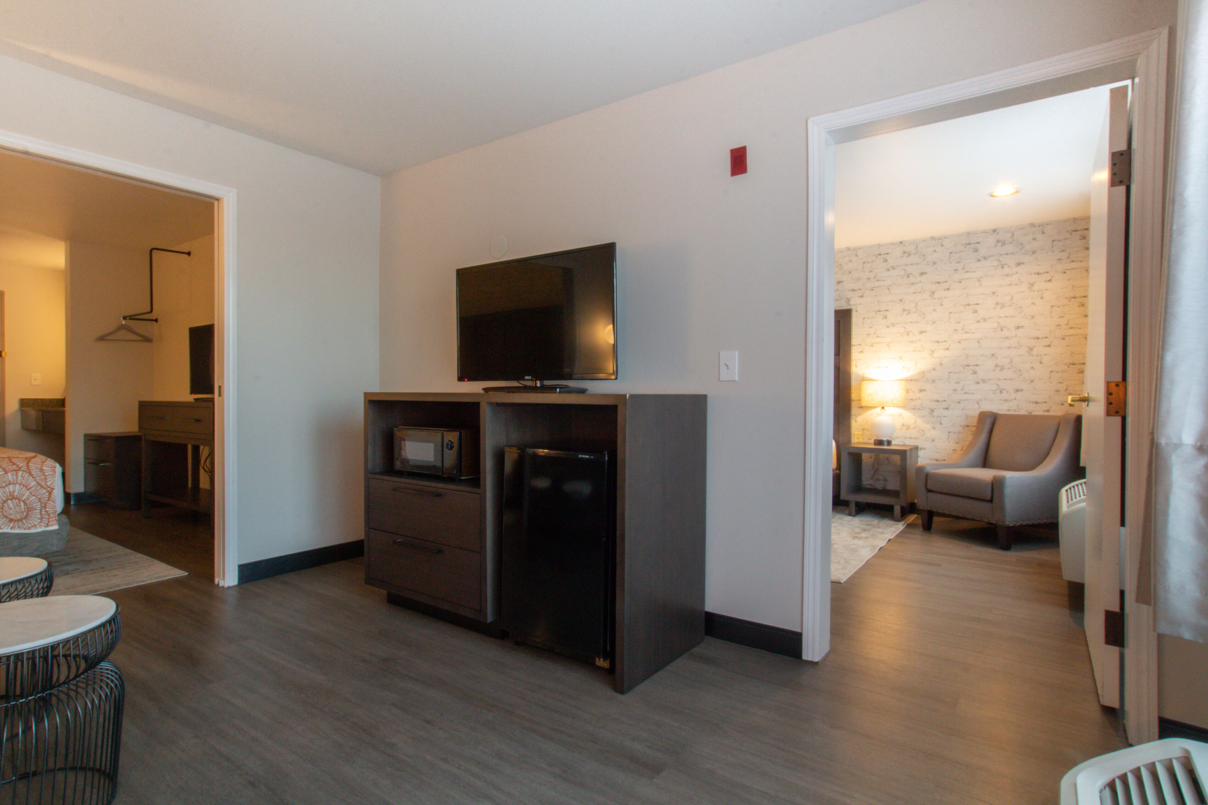 A modern living room with a flat-screen TV, a refrigerator, and a microwave. There is a dining area with a table and chairs.