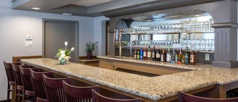 A bar area with a granite countertop, bar stools, and a glass display case filled with bottles and glasses.