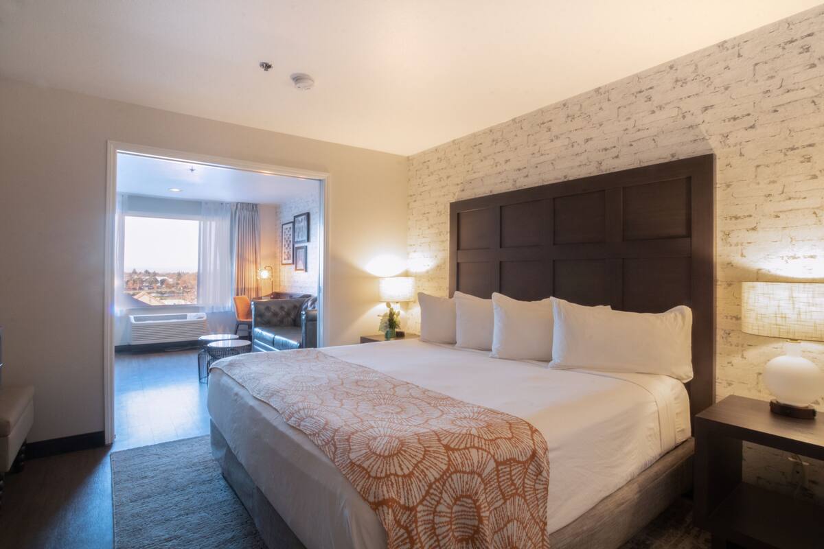 Une chambre d’hôtel avec un grand lit, une table de chevet, une chaise et une vue sur l’extérieur grâce à une porte ouverte.