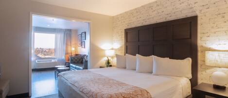 Habitación de hotel con una cama grande, una mesita de noche, una silla y vistas a través de una puerta abierta.