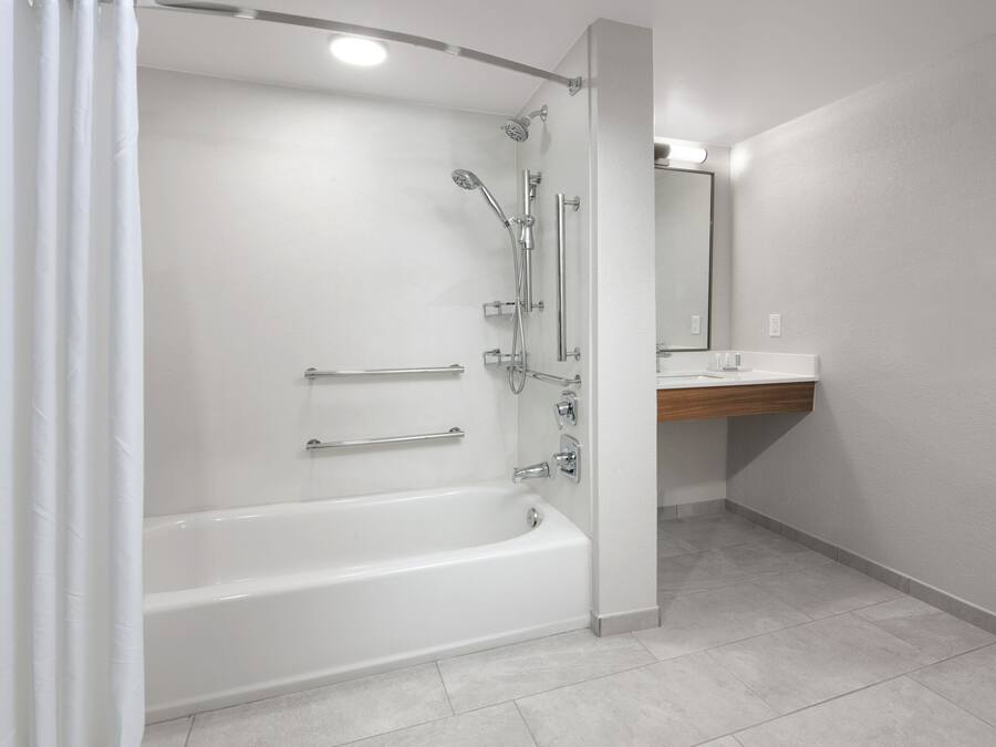Uma casa de banho moderna com uma banheira branca, chuveiro com vários jatos e toucador de madeira com espelho.