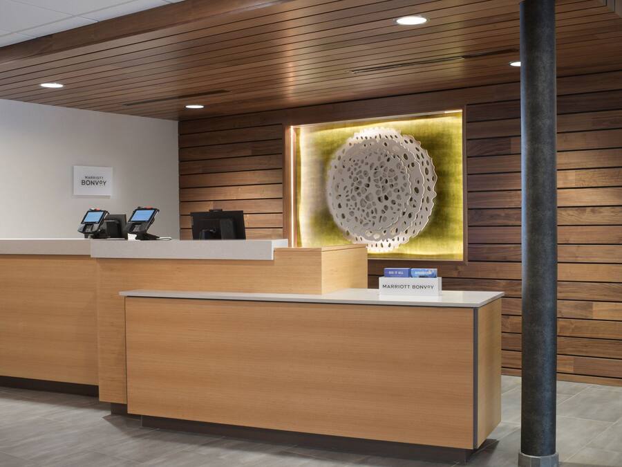 A reception desk with a wooden finish, a digital kiosk, and a decorative wall piece.