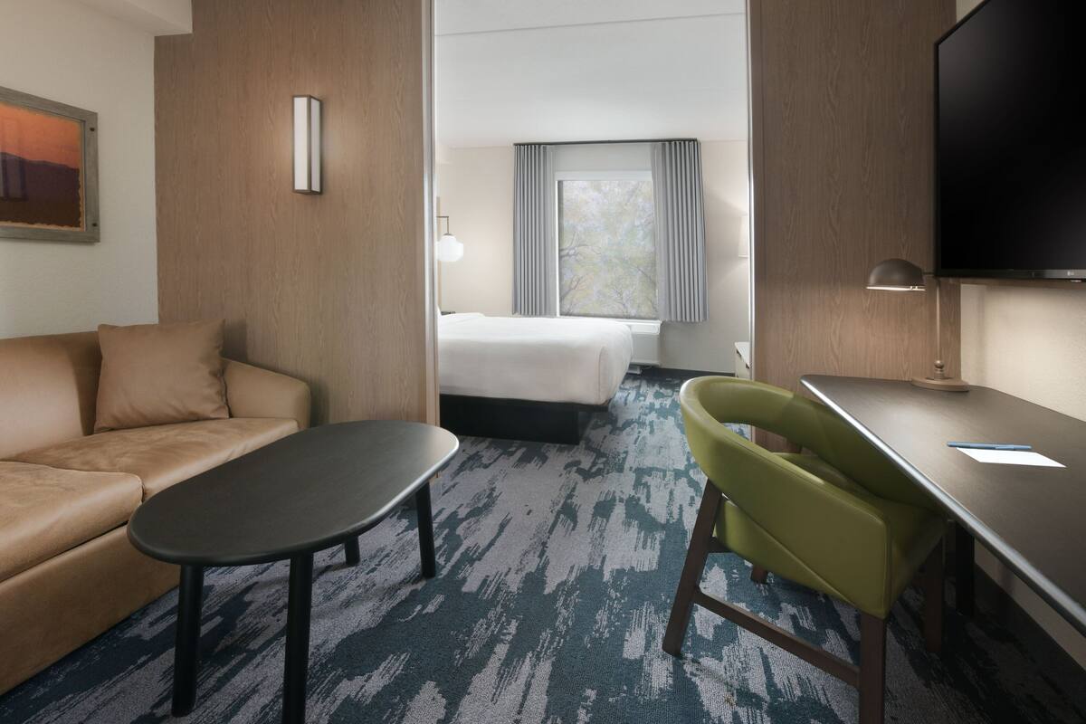 A hotel room with a bed, a sofa, a desk, and a television.