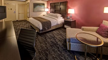A hotel room with a bed, a desk, a chair, a small table, and a TV.