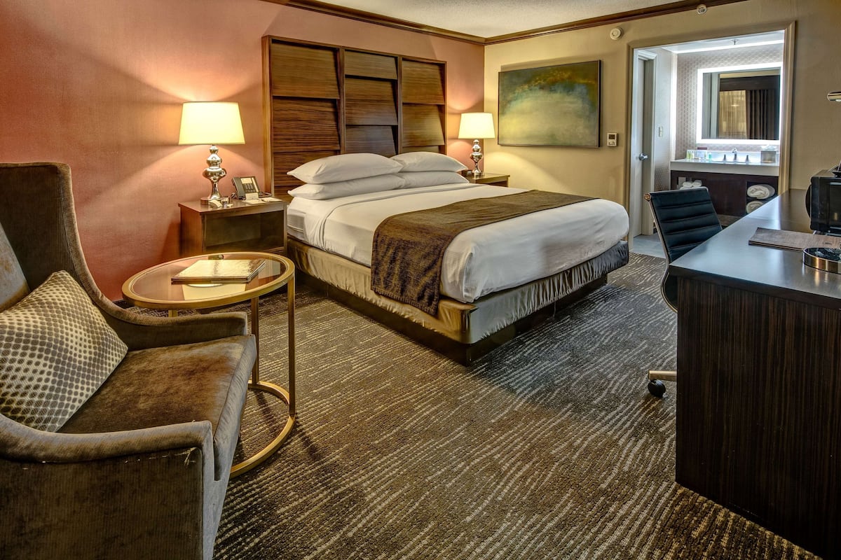 A hotel room with a bed, a desk, a chair, a round table, and a sofa.