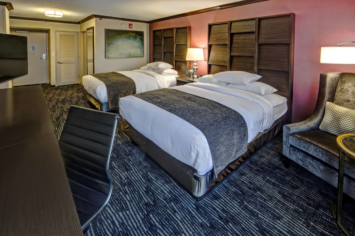 A hotel room with two beds, a desk, a chair, a TV, and a painting on the wall.