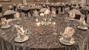Un salón de banquetes con mesas redondas dispuestas para un evento formal, con manteles blancos, cristalería y velas.