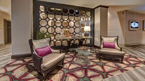 A lobby with two armchairs, a coffee table, a decorative wall, and a television screen.