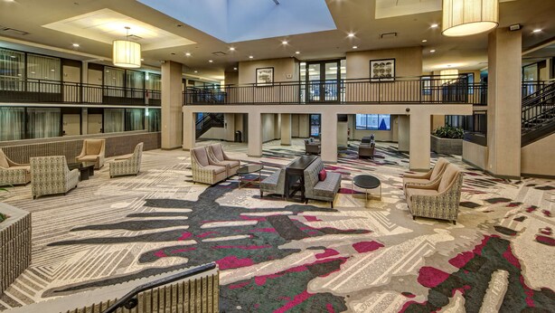 A spacious lobby with a high ceiling, multiple seating areas, and a central staircase.
