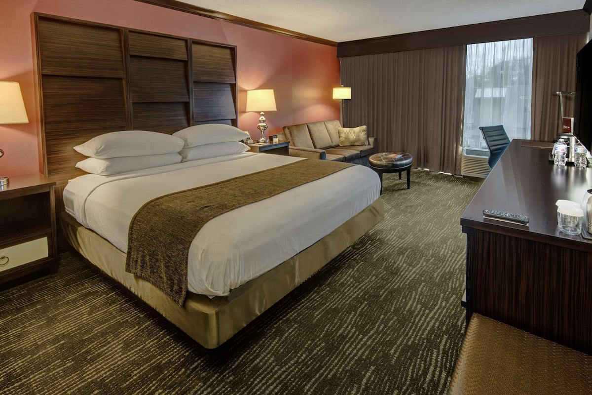 A hotel room with a large bed, two bedside tables, a desk, a chair, and a window with curtains.