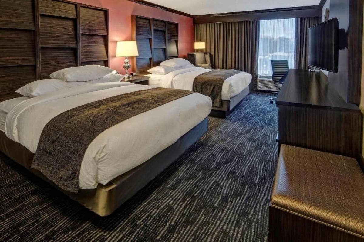 A hotel room with two beds, a desk, a TV, and a view of the city.