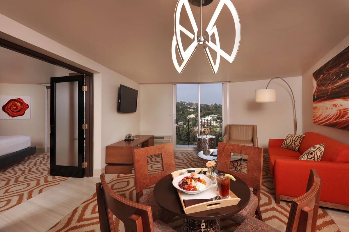 A hotel room with a dining area, a sofa, a TV, and a view of the city.