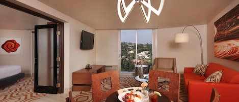Habitación de hotel con comedor, sofá, televisor y vista a la ciudad.