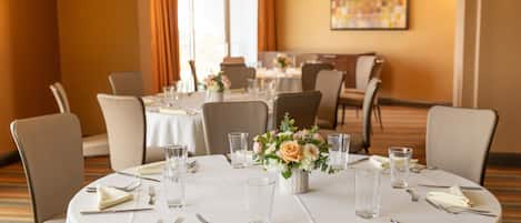 A conference room with round tables, chairs, and a floral centerpiece.
