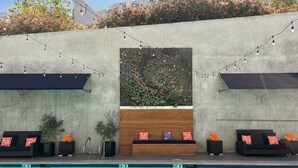 A poolside area with a wooden bench, two black lounge chairs with red and white patterned cushions, and string lights. - Hotel Angeleno (Los Angeles)