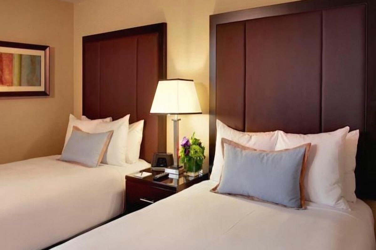 A hotel room with two beds, a nightstand with a lamp, and a framed picture on the wall.