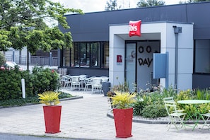 Entrada de un hotel con letrero, asientos al aire libre y plantas en macetas.