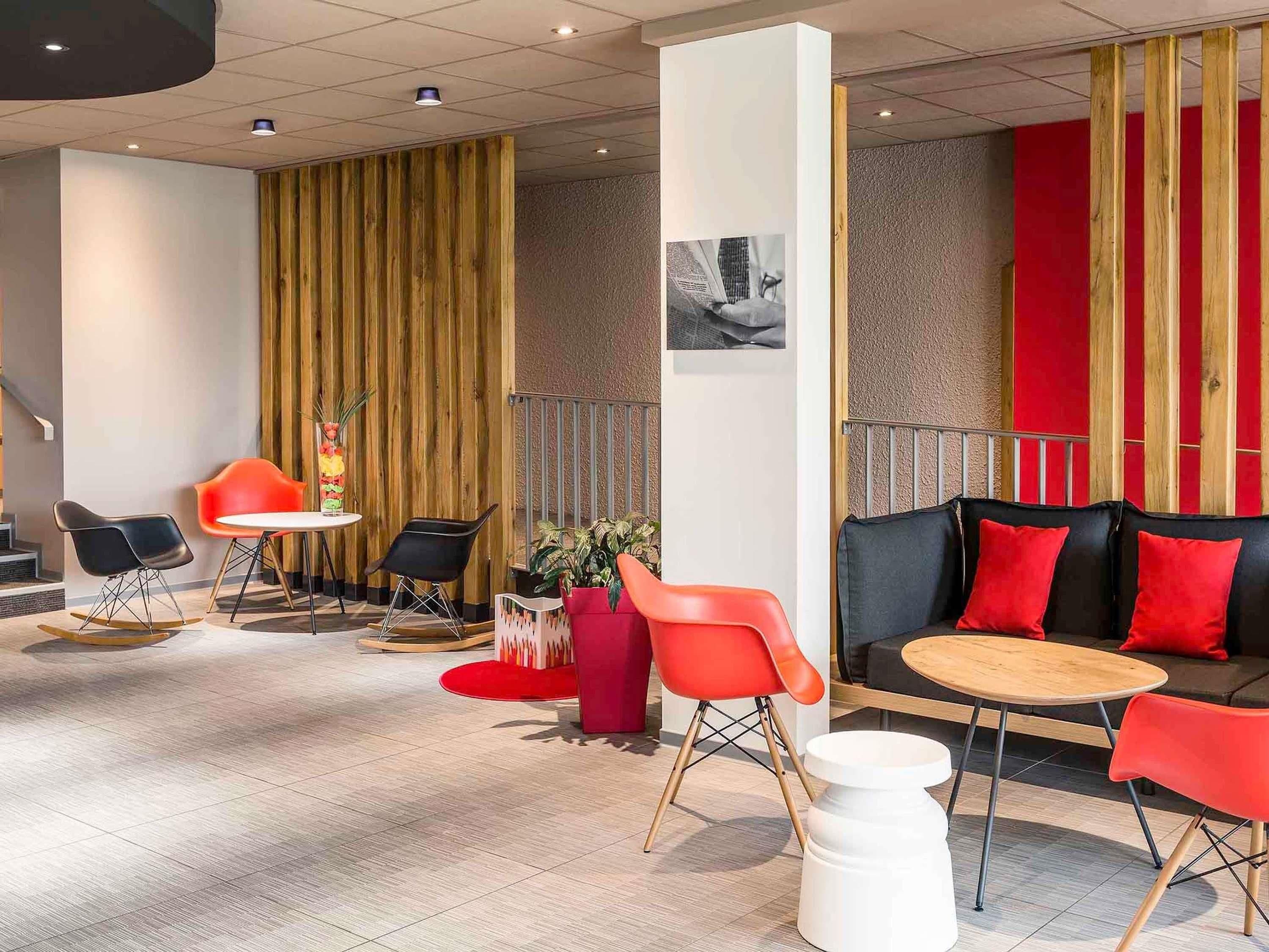 Un interior moderno con un sofá, sillas rojas, una mesita redonda y una planta decorativa.