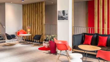 Un interior moderno con un sofá, sillas rojas, una mesita redonda y una planta decorativa.