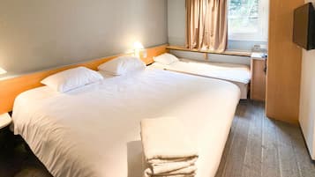 Quarto de hotel com uma cama grande, duas camas menores, uma escrivaninha, uma cadeira, uma televisão e uma janela com cortinas.