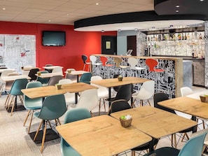 Ett modernt kafé med flera bord och stolar, en bardisk med en unik svartvit väggmålning och en platt-TV som är monterad på väggen.